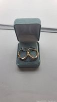 Pair of 10kt tri-color gold hoop earrings in green jewelry box, showing front view with yellow, rose, and white gold details.