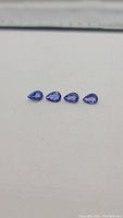 Four pear cut tanzanite gemstones arranged in a row on a white surface, front view.