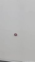 Close-up photo of a small bright pink oval spinel gemstone on a white background showing the color and cut.