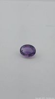 Oval facet-cut purple amethyst gemstone on white background, showing deep purple and pink bi-colored tones.
