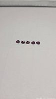 Five pear-shaped, blood red rubies arranged in a line on a white surface, clear and focused, showing their shape and color.