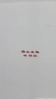 Seven natural marquis cut sapphires arranged on a white background, colors deep pink to orange hues.