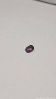 Oval natural deep pink reddish spinel gemstone placed on white surface showing color and facets under light