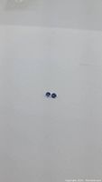 Pair of small round blue-violet diamond cut Tanzanite stones on a white background.