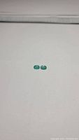 Pair of small oval cabochon emeralds in green color on white background.