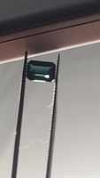 Emerald cut deep blue-green tourmaline gemstone held by tweezers against a light background showing its color and cut