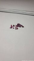 Lot of 12 natural ruby crystals spread on a white surface, showing size and color variation including one large deep red crystal and smaller ruby pieces