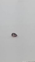 Single pear cut purple Tourmaline gemstone with visible pink and orange color flashes on a white background.