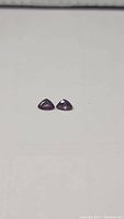 Two matching trillion cut fancy colored sapphires displaying red, orange, pink and purple hues on a white background.