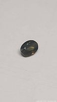 Oval cut tri-colored sapphire stone displaying green, yellow, and orange hues on flat white background.