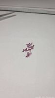 Multiple small faceted rhodolite garnet gemstones scattered on a white surface, showing their pink to purple color and diamond cuts.