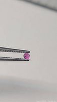 Round cut ruby gemstone held with tweezers showing deep pink to red natural color