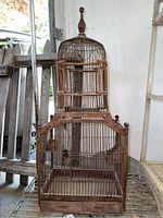 Full front view of tall antique wooden and wire birdcage with rounded dome top and wooden finial, showing wire cage and wooden frame base.