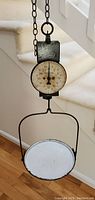 Full view of the antique hanging hook weight scale with chain and metal weighing dish shown full length suspended.