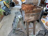 Photo showing two weathered wooden step stools and large Canada Dry wood crate on a stand.