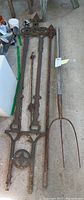 Cast iron trellis with two posts alongside pitch fork, showing overall length and ornate design details.