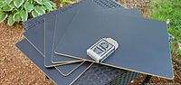 Five rectangular black chalkboard placemats stacked with cork backing visible on one edge and black writing surface on top, placed outdoors.