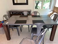 Front view photo capturing the rectangular table with metal top and wooden legs along with six gray metal dining chairs around it.