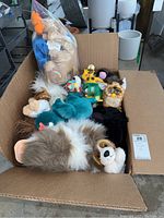 View of full box showing a Furby toy, multiple stuffed animals and Simpsons figurines inside a cardboard box.