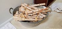 Side view of galvanized metal wash tub filled with birch kindling bundles, showing peeling white bark of birch branches.
