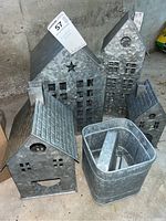 Photo showing four galvanized aluminum house-shaped lanterns of varying sizes arranged together next to a rectangular galvanized canister.