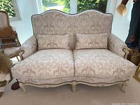 Full front view of the loveseat showing scalloped back, rolled arms, carved wood frame and two seat cushions with lumbar pillows in place