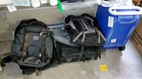 Photo showing multiple bags including backpacks and cooler on garage floor