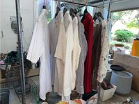 Photo showing a rack of men's and women's tops in light and neutral colors, mostly size medium, hung on hangers.