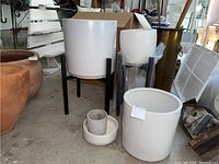 Two black metal stands with white planters, plus three planters on floor