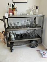 Full front view of three-tier metal bar cart loaded with glassware