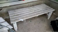 Front and top angled view of the rustic milk wash wood bench in garage showing slatted seat and rounded legs.