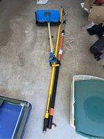Blue plastic shovel, yellow plastic shovel, Fiskars tree pruner laid on concrete floor.