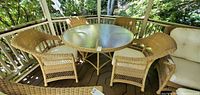 Full view of round glass-top table surrounded by four wicker armchairs on a wood deck under gazebo