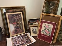 Group of assorted framed and unframed art pieces leaning against a wall