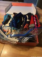 Shoebox filled with folded scarves in various colors and patterns, some scarves loosely arranged on top, including a blue silk-like scarf and a red patterned scarf.
