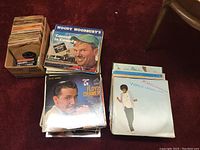 Three piles of assorted vinyl records including artists Woody Woodbury, Floyd Cramer, and Joan Armatrading.