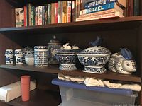 Shelf showing blue and white ceramics including multiple covered jars and animal-shaped containers with blue patterning