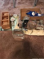 Photo showing a variety of costume jewelry, a small wooden organizer, glass vanity items, and a brown leather coin purse all placed on a carpeted floor