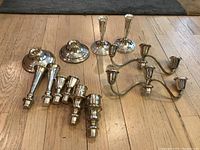 All 12 candlestick pieces arranged on wood floor, showing variety of bases, holders, and candelabra parts
