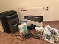 Photo shows Royal 14 sheet crosscut paper shredder, Bose Solo TV sound system box, various small electronics and accessories including a camera box, Panasonic phone, and other items on floor.