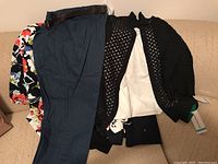 Piled Alfred Dunner clothing showing black knit cardigan, white top, navy pants with belt, and floral print blouse underneath.