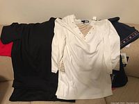 Four women's tops laid out flat, showing black, white, red, and navy blue tops with tags visible on some.