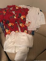 Photo showing red floral Hawaiian short-sleeve shirt along with multiple white tops and white pants laid out on chair, new with tags.