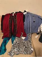 Photo showing several folded women's clothing items including a red embroidered cardigan, black and white patterned dress or skirt, light blue zip-up jacket, and blue patterned pants.