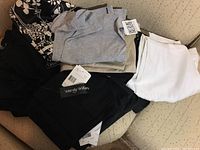 Photo showing several pairs of pants in black, gray, and white colors, on a light colored couch. Tags visible from Wendy Williams and Rojos among others.