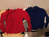 Photo showing red button-up sweater over colorful striped and yellow sweaters with tags