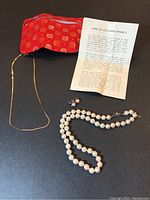 Full set of items displayed: cultured pearl necklace, matching pearl earrings, thin 14K Italy gold chain, and care instructions leaflet on a dark surface.