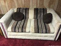 Front view of the smaller couch showing beige fuzzy exterior and striped cushions with two brown round pillows.