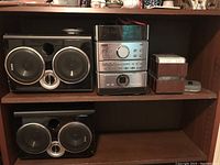 Wide shot of RCA RS2032 stereo system with dual speakers and cassette tapes on wooden shelf