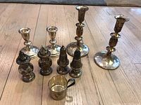 Photo showing all 9 items: 4 candlestick holders, 4 salt and pepper shakers, and 1 baby cup, all tarnished and showing age wear.